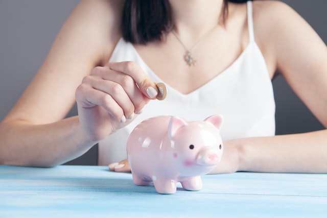 woman in a white tank top holding a coin over a pink piggy bank